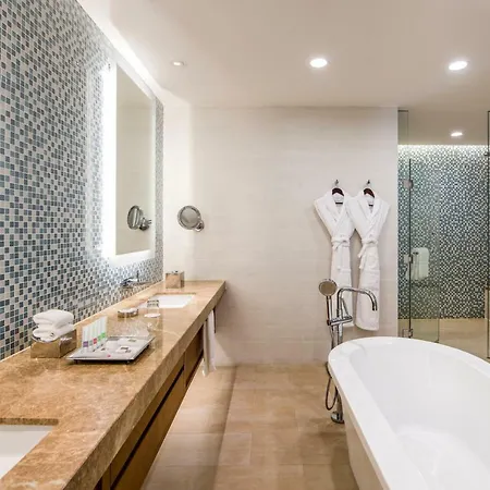 Swissotel Al Ghurair Dubai - Deira & Creek Exterior photo The photo shows a modern bathroom featuring a large white bathtub, a stylish wooden vanity with a marble countertop, and dual mirrors above it. The walls are adorned with blue mosaic tiles, creating a vibrant accent. Fluffy white bathrobes hang on ho